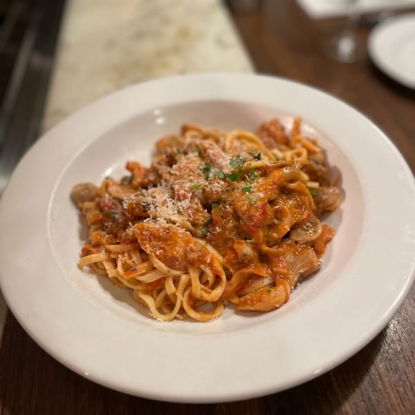 Linguine pasta with a creamy tomato sauce, mushrooms, and grated Parmesan cheese on a white plate.