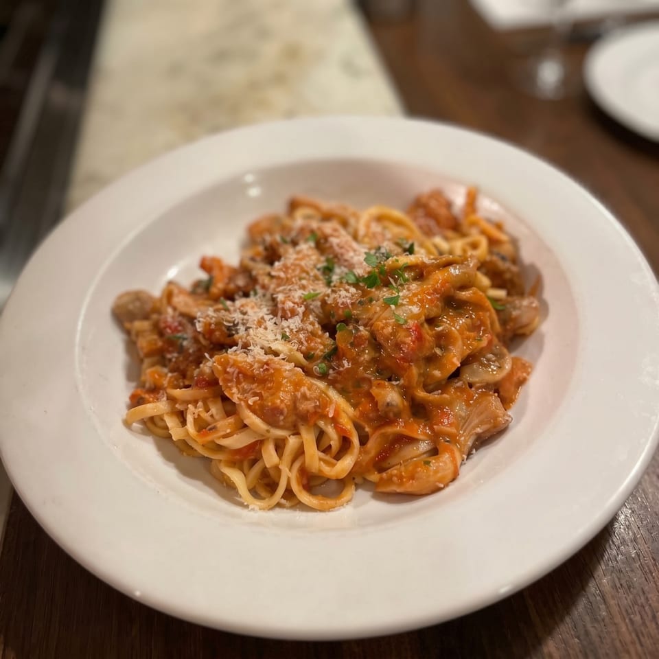 Linguine pasta with a creamy tomato sauce, mushrooms, and grated Parmesan cheese on a white plate.