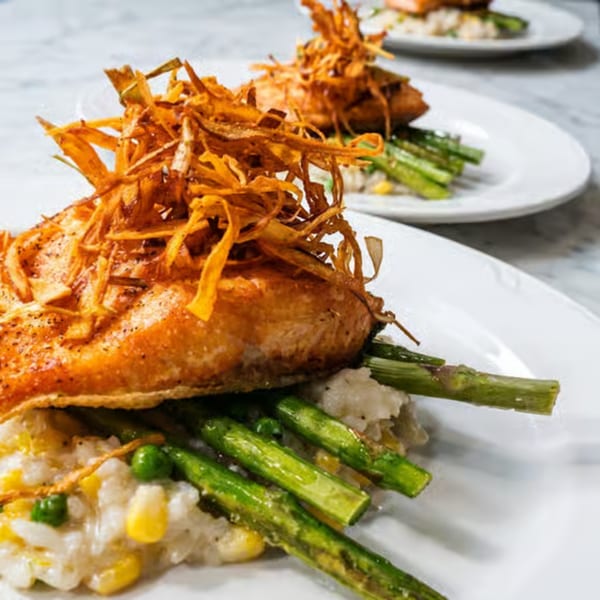 Two plates of salmon with crispy fried onions, asparagus, and risotto with corn and peas.