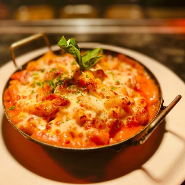 A skillet of baked gnocchi with melted cheese, tomato sauce, and basil on a white plate.