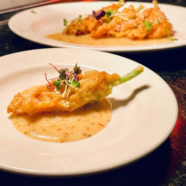 Two plates of fried zucchini blossoms with a creamy sauce and microgreens on a dark surface.